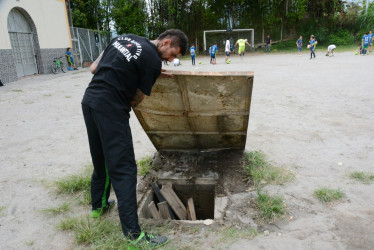 Juan Guillermo Luján Maya, entrenador asistente de fútbol, muestra el mal estado de la cancha de la vereda Alto Bonito y el peligro que representa para los niños. En un costado del escenario deportivo, hay un hueco cubierto por una lámina. La comunidad exige mantenimiento de la Alcaldía de Manizales. Sostienen que están en juego los derechos de los niños.