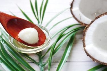 Cuchara de palo con aceite de coco al lado de un coco partido a la mitad.