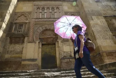 Una mujer se resguarda del sol con una sombrilla mientras camina junto a la Mezquita-Catedral de Córdoba, donde junto con Sevilla las temperaturas han subido hasta una máxima de 37 grados, según la predicción de la Agencia Estatal de Meteorología (AEMET).