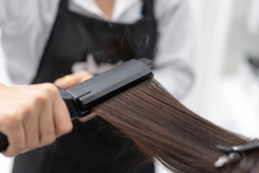 Estilista le plancha el cabello a una mujer.