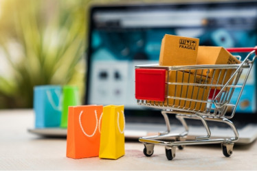 Carrito de compras con bolsas adentro con un computador portatil detrás