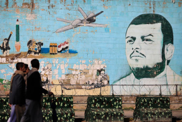 Unas personas pasan junto a un mural en una pared que representa al líder de los hutíes, Abdul-Malik al-Houthi, un dron y un misil. 