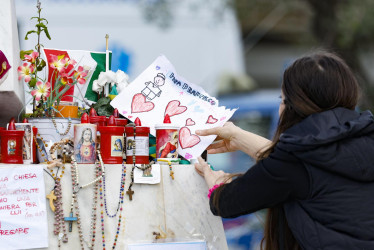 Una mujer coloca un dibujo del papa Francisco al pie de la estatua del papa Juan Pablo II, frente al Hospital Universitario Gemelli de Roma.