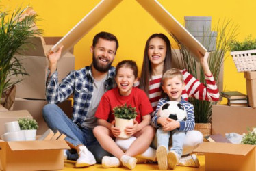 Familia feliz sentada bajo un cartón al lado de muchas cajas.