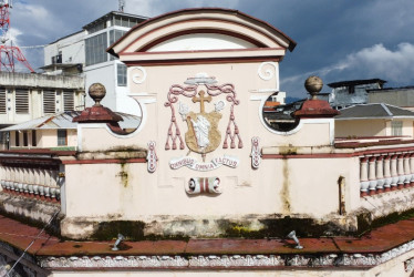 En lo alto de la fachada del Palacio Arzobispal se destaca el escudo episcopal de monseñor Tiberio de Jesús Salazar, obispo de Manizales entre 1922 y 1932, con la frase en latín Omnibus Omnia Factus (Todo lo hecho para todos). Este lema resume el espíritu de servicio de la Iglesia y su papel en la sociedad. Como muchos otros anagramas y escudos del Centro Histórico es símbolo de identidad, linaje y poder en la arquitectura republicana de la ciudad.
