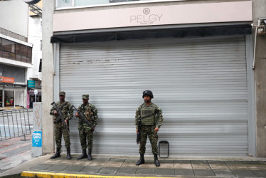 Integrantes de Fuerzas Armadas vigilan un área frente a locales comerciales cerrados este miércoles, en el centro de Cali (Colombia).
