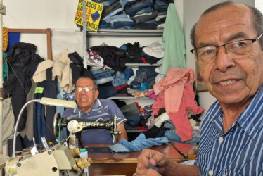 Wlfredo tienen a su espalda un bulto de ropa que ha reparado. Su hermano Norman mira a la cámara de LA PATRIA para registrar el momento. 