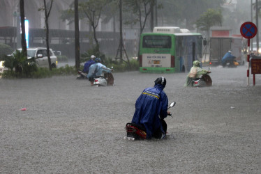 La gente se transporta con sus motos por una calle inundada en Hanoi (Vietnam).