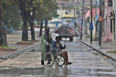 Personas se protegen de la lluvia este martes, en Santiago de Cuba (Cuba). 
