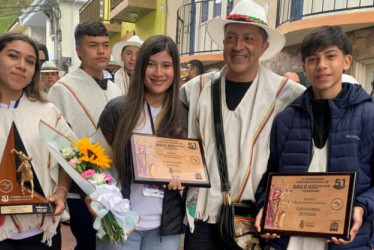 El director de la banda sinfónica estudiantil del Instituto Neira, Holver Mauricio Cardona, en compañía de algunos músicos quienes exhiben los reconocimientos obtenidos en Paipa (Boyacá). 
