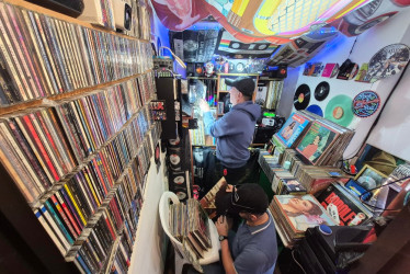Guillermo Osorio Díaz revisa su colección de discos en Archivo Musical, su pequeño local en Manizales conocido como “El Búnker del Vinilo”, mientras su cliente Wilmar Ortiz Buriticá se arrodilla para buscar entre los LP clásicos que mantienen vivo el gusto por el formato físico.