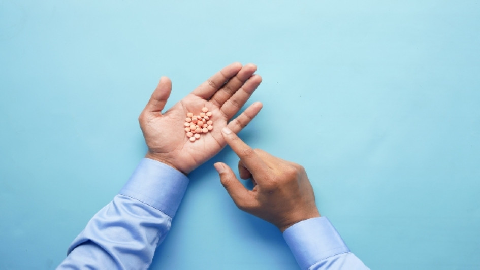 Hombre con mangas azules con pastillas en una mano señalándolas con la otra mano.