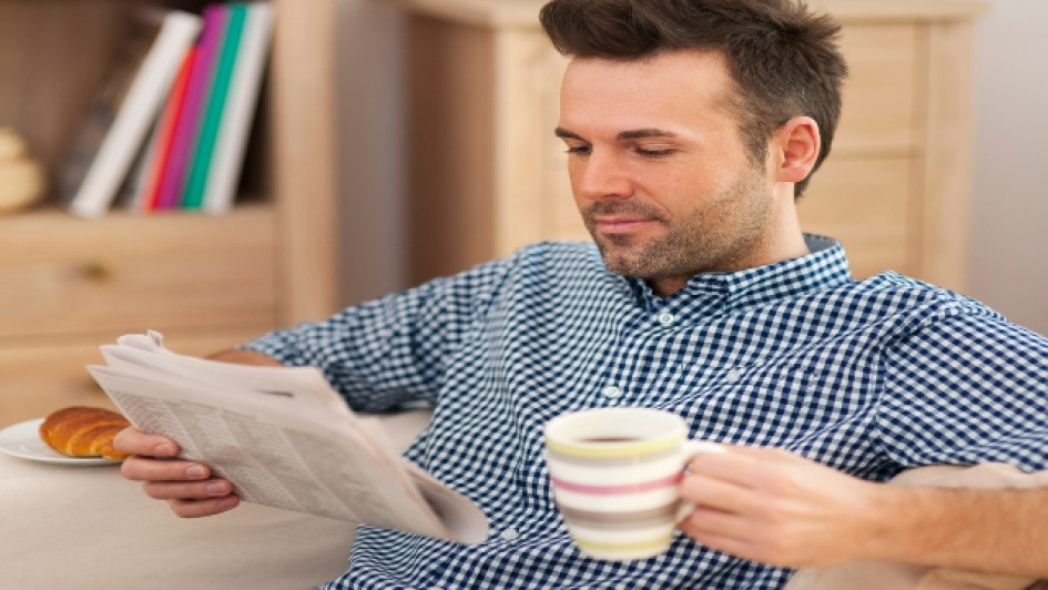 Hombre sonriente leyendo el periódico con una taza de café.