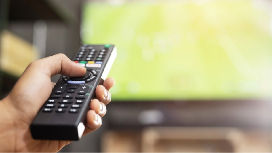 Mano sosteniendo un control de TV con el TV de fondo