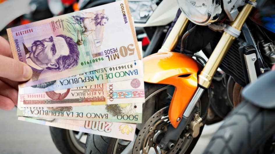 Mano sosteniendo billetes de pesos colombianos frente a varias motos.