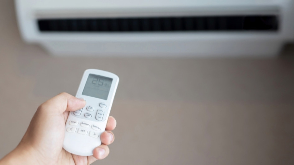 Persona sosteniento un control remoto de aire acondicionado con el aire acondicionado en el fondo.