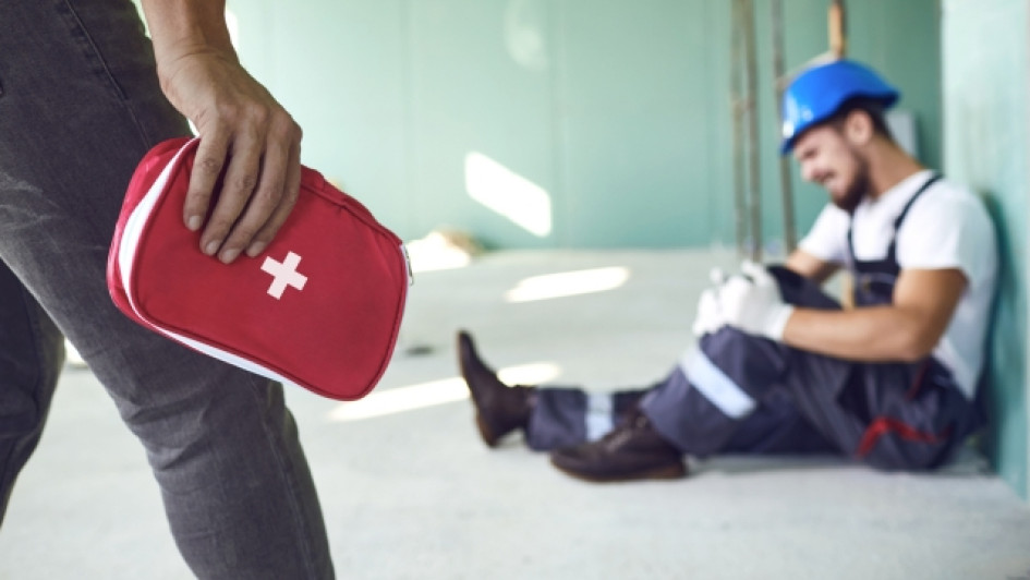 Persona con un botiquín se acerca a un trabajador que está adolorido en el piso.