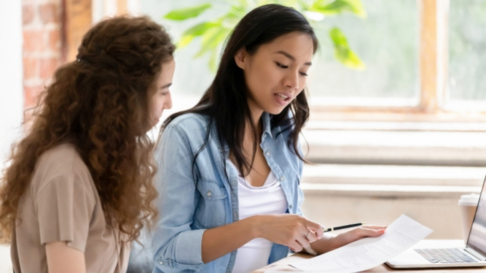 Dos mujeres sentadas en un escritorio revisando unos papeles.