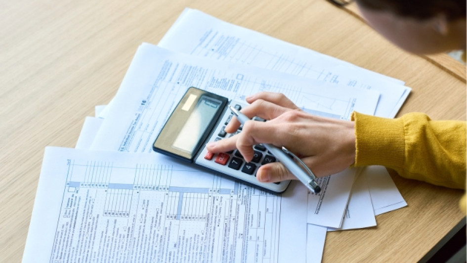 Mano usando una calculadora encima de unos papeles