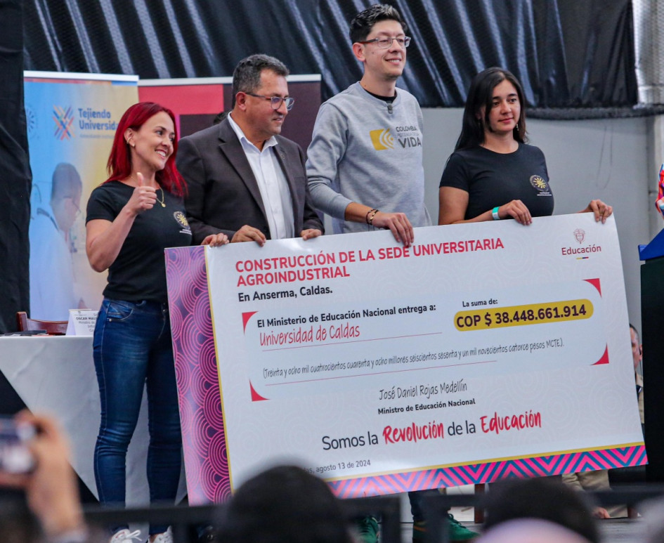El rector de la Universidad de Caldas, Fabio Hernando Arias (izq.), y el ministro de Educación Nacional, Daniel Rojas, sostienen el cheque que certifica la inversión de $38 mil millones para la construcción de la sede agroindustrial de la institución en Anserma. Los acompañan las estudiantes Yeimi Quintero y Érika Sánchez.