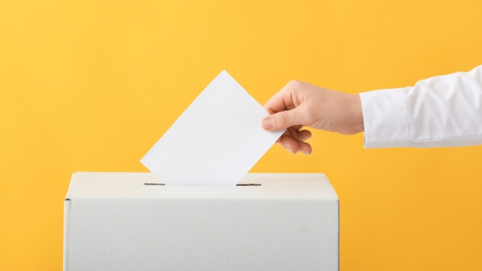 Meno introduciendo un voto en una caja. Fondo amarillo.