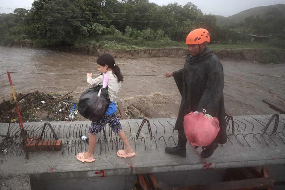 Un integrante del cuerpo de socorro de Honduras ayuda a una niña a evacuar debido a las crecidas de ríos y quebradas por el paso de la tormenta Sara. 