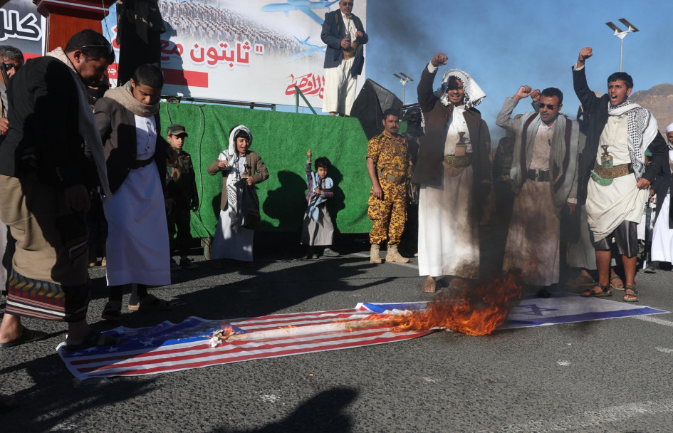 Partidarios hutíes queman una pancarta con banderas estadounidenses e israelíes durante una protesta contra esos países en Yemen.