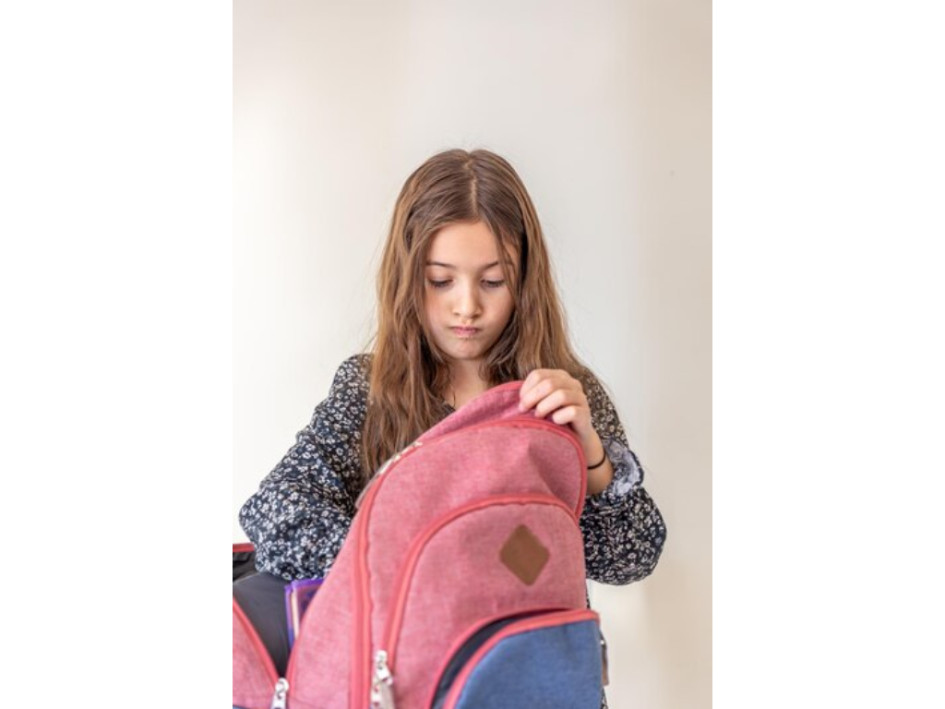 Niña empaca útiles escolares en su maleta.