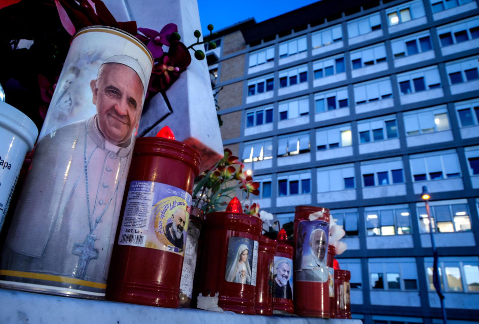 Una vela con la imagen del Papa Francisco, al pie de la estatua de San Juan Pablo II en las afueras del Hospital Universitario Gemelli, en Roma, donde el Papa Francisco se encuentra hospitalizado.