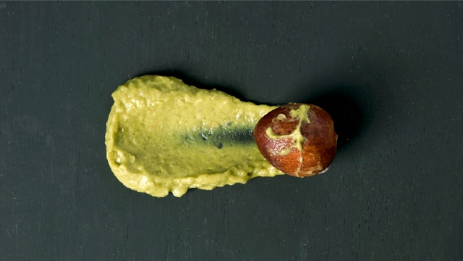 Pepa de aguacate cubierta en parte por guacamole en una superficie negra.
