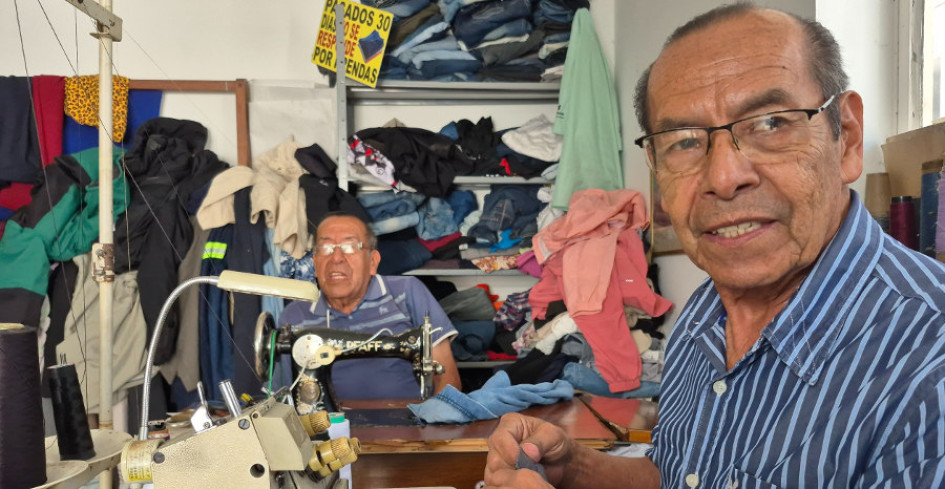 Wlfredo tienen a su espalda un bulto de ropa que ha reparado. Su hermano Norman mira a la cámara de LA PATRIA para registrar el momento. 