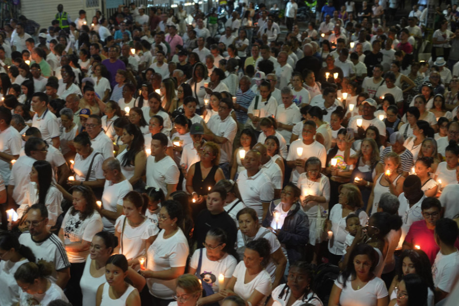 Personas vestidas de blanco sostienen velas encendidas en una 'velatón' por la paz y la memoria este domingo, frente a la Base Aérea Marco Fidel Suárez, en Cali. 