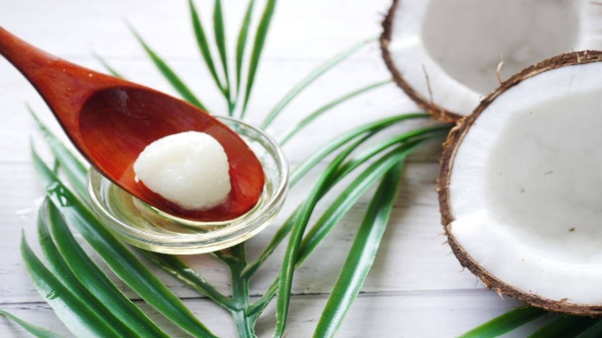 Cuchara de palo con aceite de coco al lado de un coco partido a la mitad.
