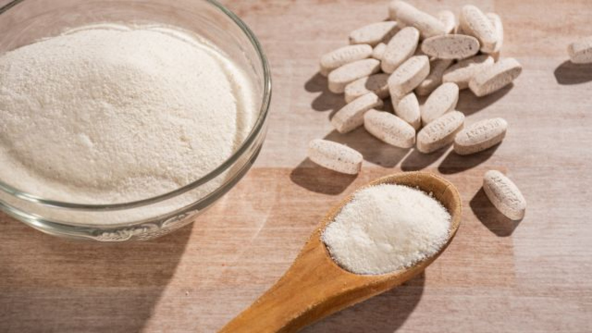 Cuchara de palo con colágeno en polvo al lado de pastillas de colágeno y colágeno en polvo en un bowl.