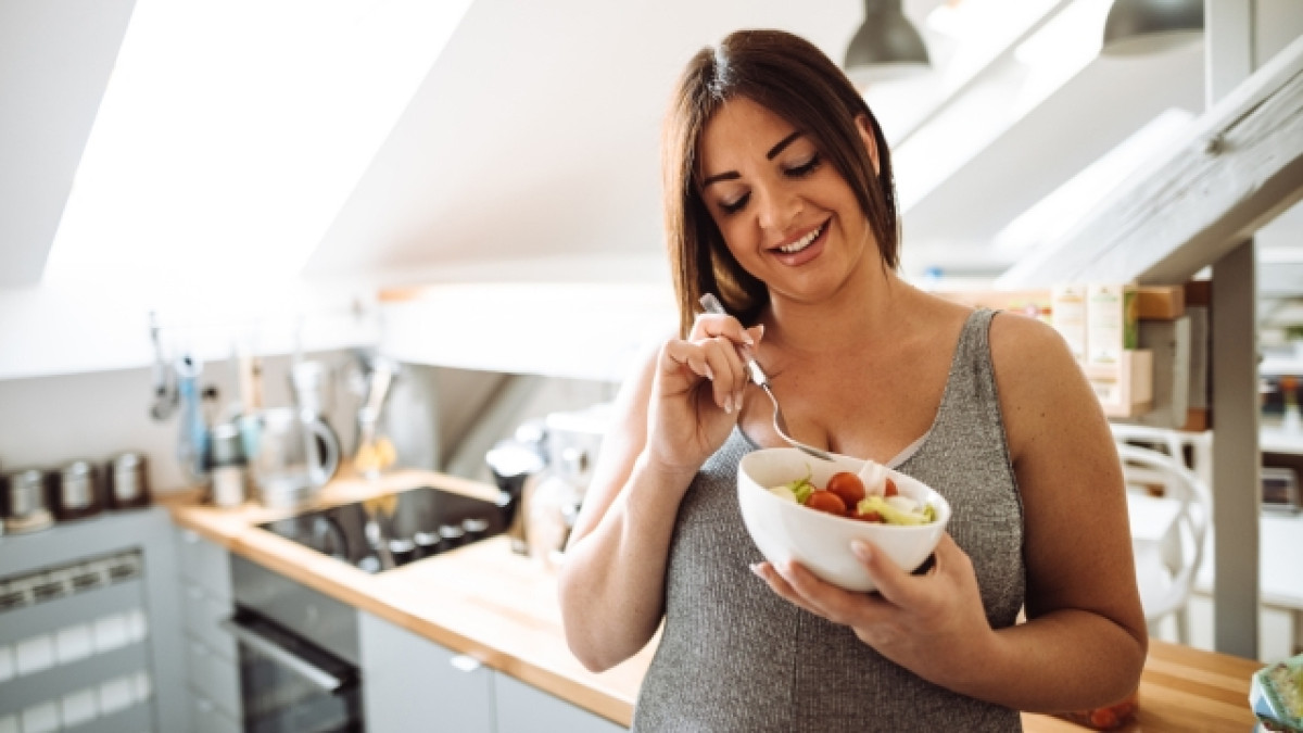 Mujer embarazada comiendo de un bowl en una cocina.